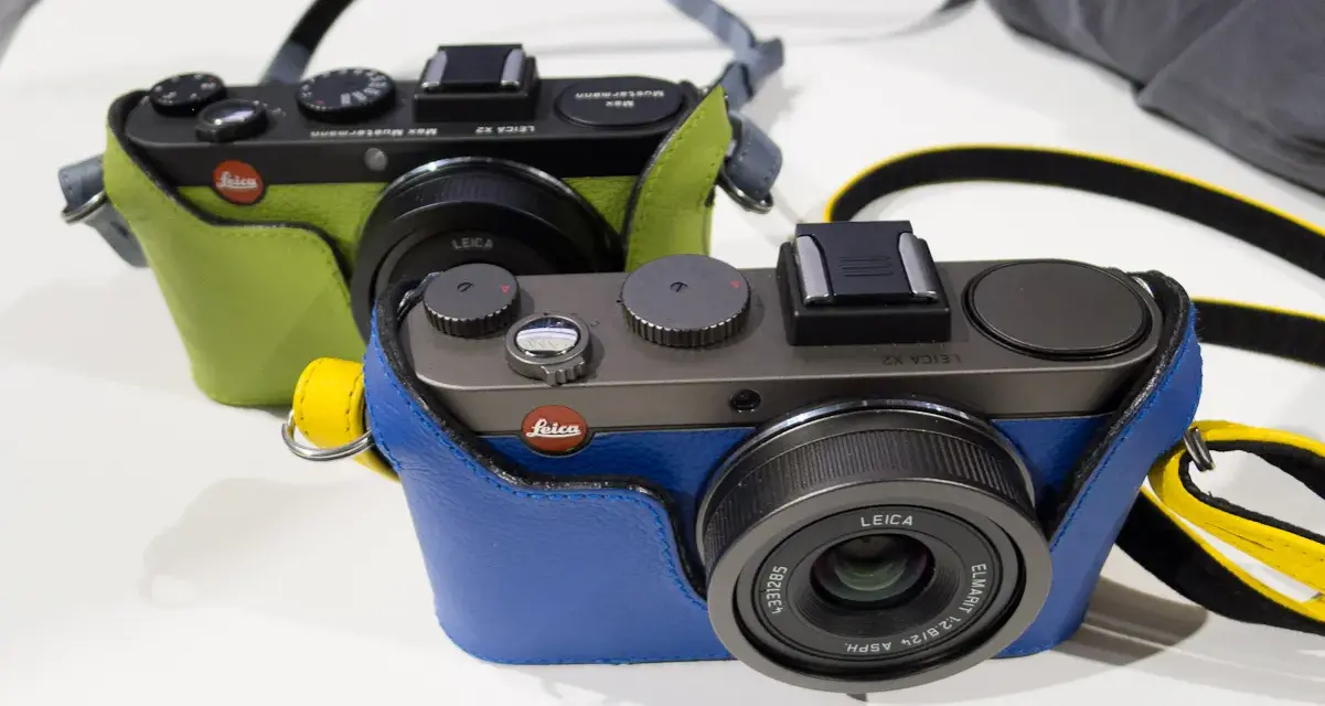 Dwie stylowe Leica X2 w kolorowych futerałach: jedna zielona, druga niebieska. Idealne do uchwycenia każdej chwili.