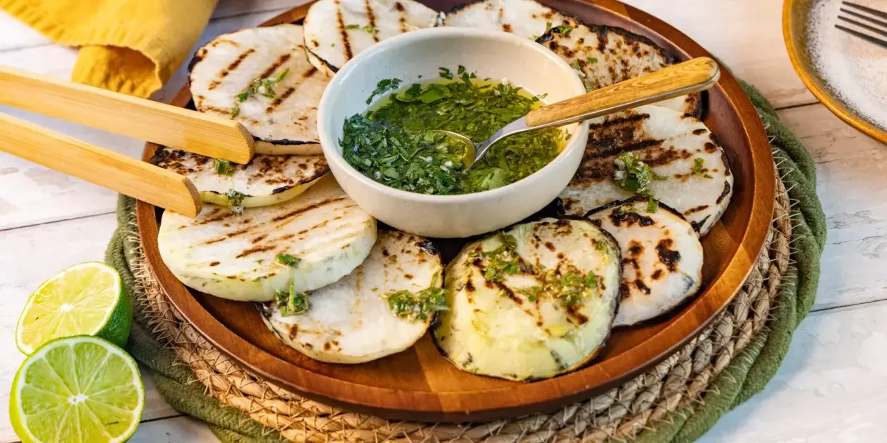 Gegrillte Kohlrabi-Scheiben mit Kräuter-Dressing und Limettenspalten auf einem Holzteller. Ein köstliches Gericht, das Lust auf Kohlrabi grillen macht.