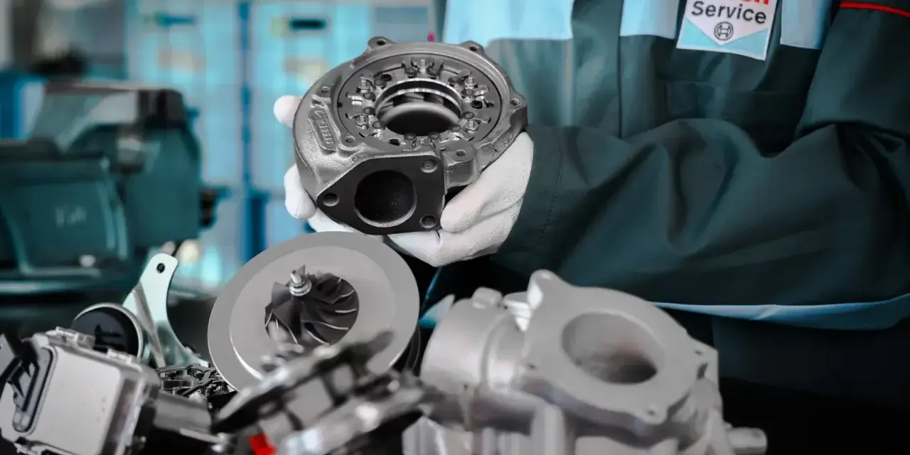 Mechanik w fartuchu Bosch Service prezentuje części turbosprężarki. Rozpoznaj uszkodzona turbina objawy i zgłoś się do serwisu.