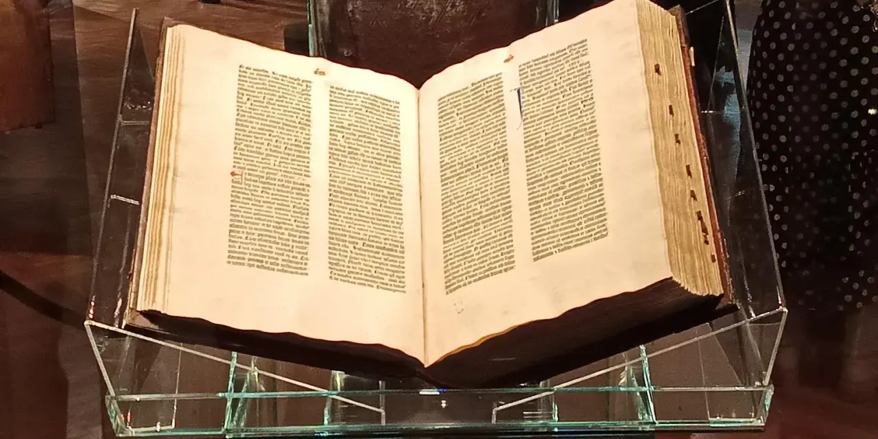 Otwarta biblia gutenberga pelplin, prezentowana na szklanym stojaku, świadectwo historii druku.