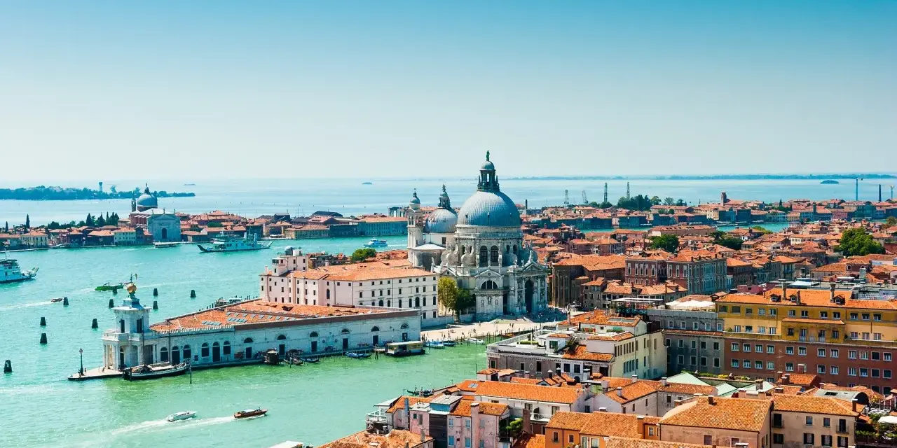 Venezia, con la sua Basilica di Santa Maria della Salute e i canali vibranti, offre infinite curiosità. Le case colorate e i tetti rossi si specchiano sull'acqua.
