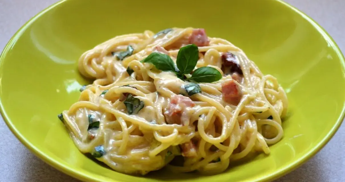 Spaghetti carbonara ze śmietaną, podane w zielonej misce, udekorowane bazylią. Pyszny przepis na klasyczne danie.