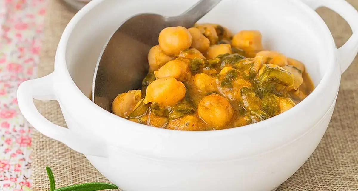 Un tazón blanco lleno de garbanzos con acelgas, un plato reconfortante y nutritivo.