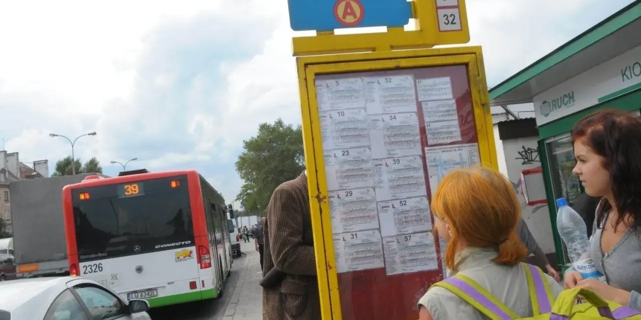 Ludzie sprawdzają 79 rozkład jazdy na przystanku. Autobus linii 39 stoi obok.