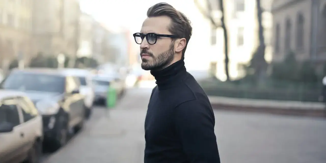 Elegancki mężczyzna w czarnym golfie i okularach, zamyślony, jakby planował zagrywki zakochanego faceta.