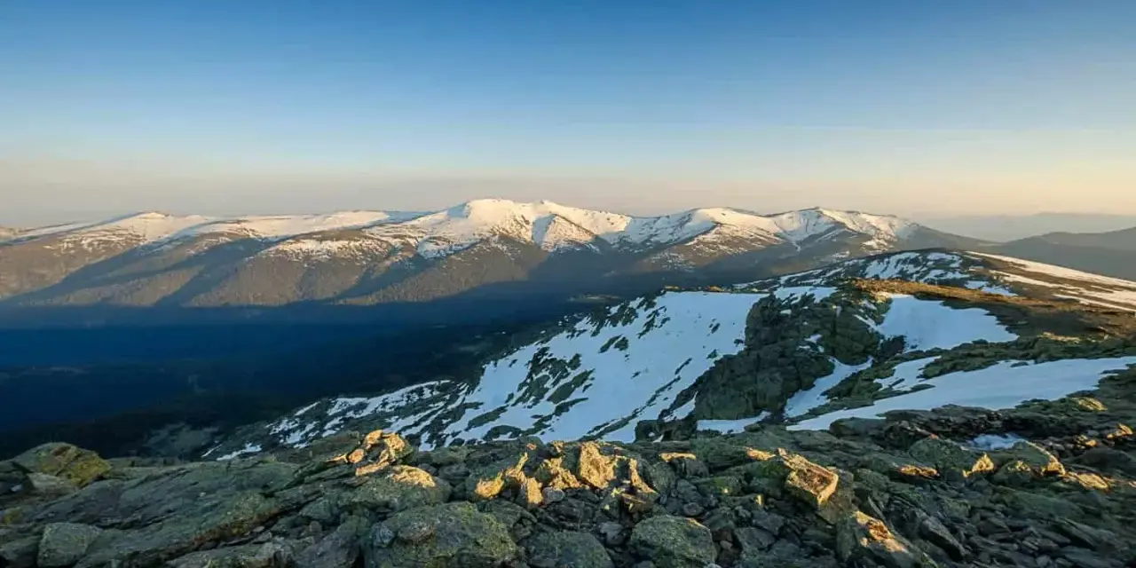 Paisaje montañoso nevado al amanecer, con rocas en primer plano y el pico Madrid en la distancia.