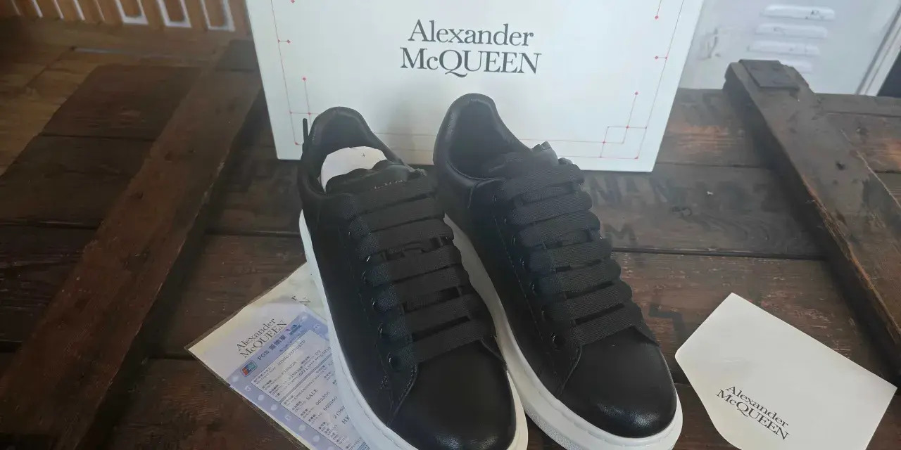 Czarne sneakersy Alexander McQueen na grubej, białej podeszwie, obok pudełka z logo marki.
