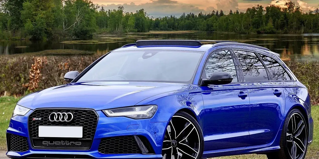 Niebieski **hatchback** z napędem quattro, zaparkowany nad jeziorem, z pięknym zachodem słońca w tle.
