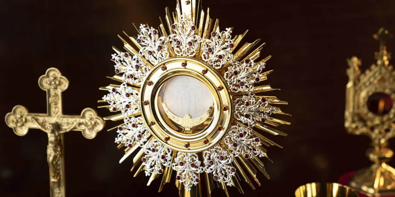 A golden monstrance holds the blessed sacrament, surrounded by ornate details and red jewels. A crucifix stands nearby, a symbol for a blessed sacrament prayer request.