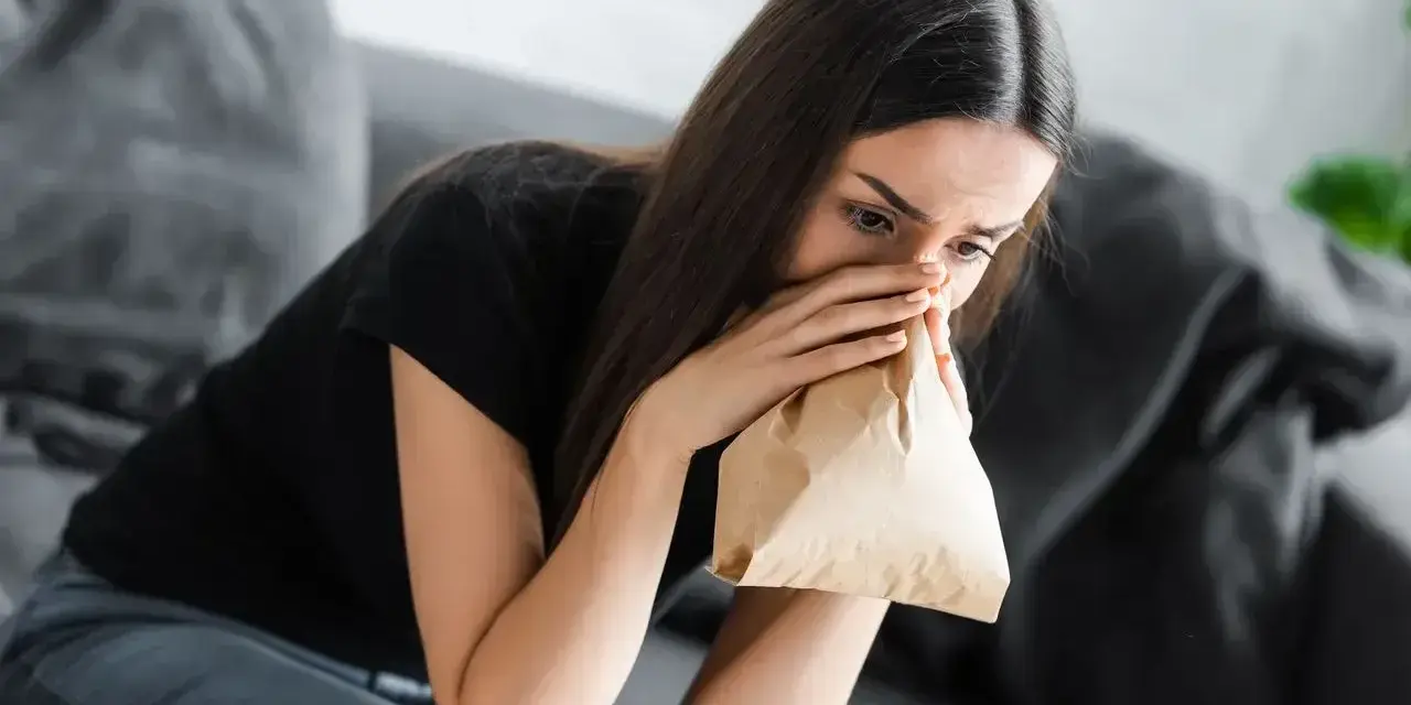 Kobieta z papierową torbą przy ustach, próbująca opanować hiperwentylację.