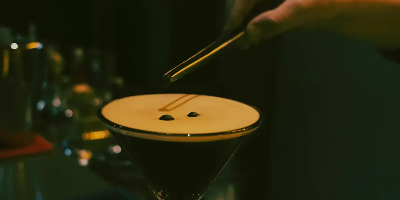 En hand lägger kaffebönor på en krämig espresso martini.