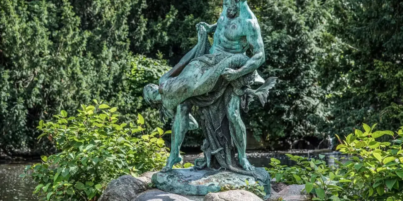 Bronzestatue eines Mannes, der eine Frau trägt, vor einem grünen Hintergrund mit einem kleinen Wasserfall in Berlin.