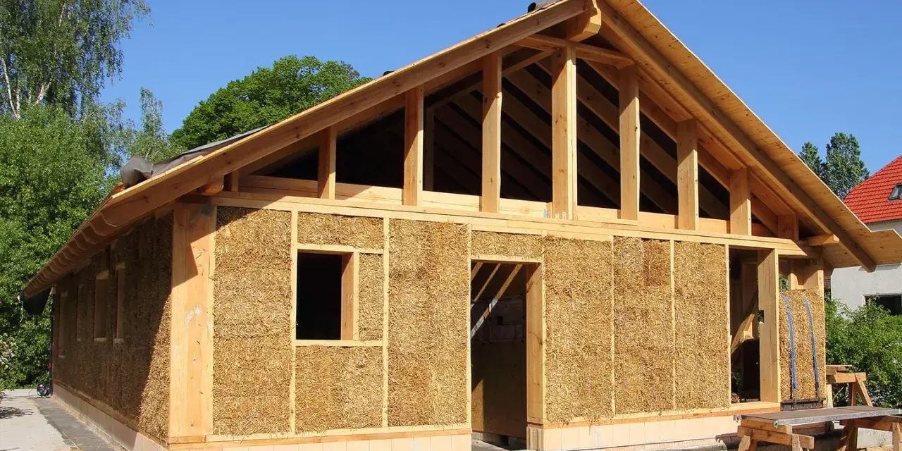 Construction d'une maison en paille écologique, avec une structure en bois visible et des murs isolés en bottes de paille.