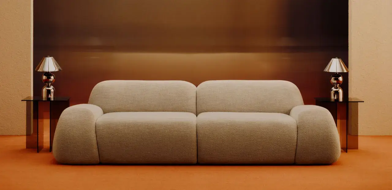 Divano beige bouclé, un materiale morbido e accogliente, con tavolini neri e lampade cromate.