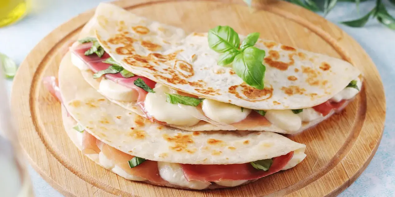 Piadina come farcirla: prosciutto, mozzarella filante e basilico fresco, un'idea gustosa e veloce.