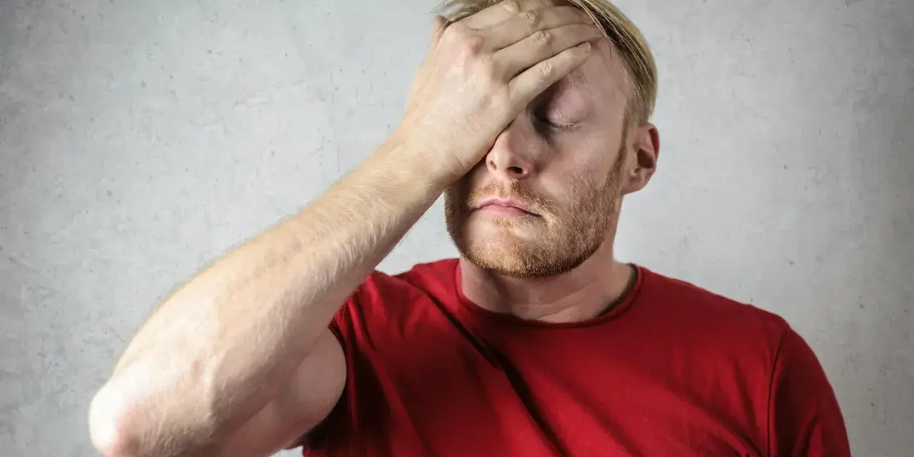 Uomo con mano sulla fronte, occhi chiusi, espressione di stress. Possibili sintomi di attacchi epilettici da stress.