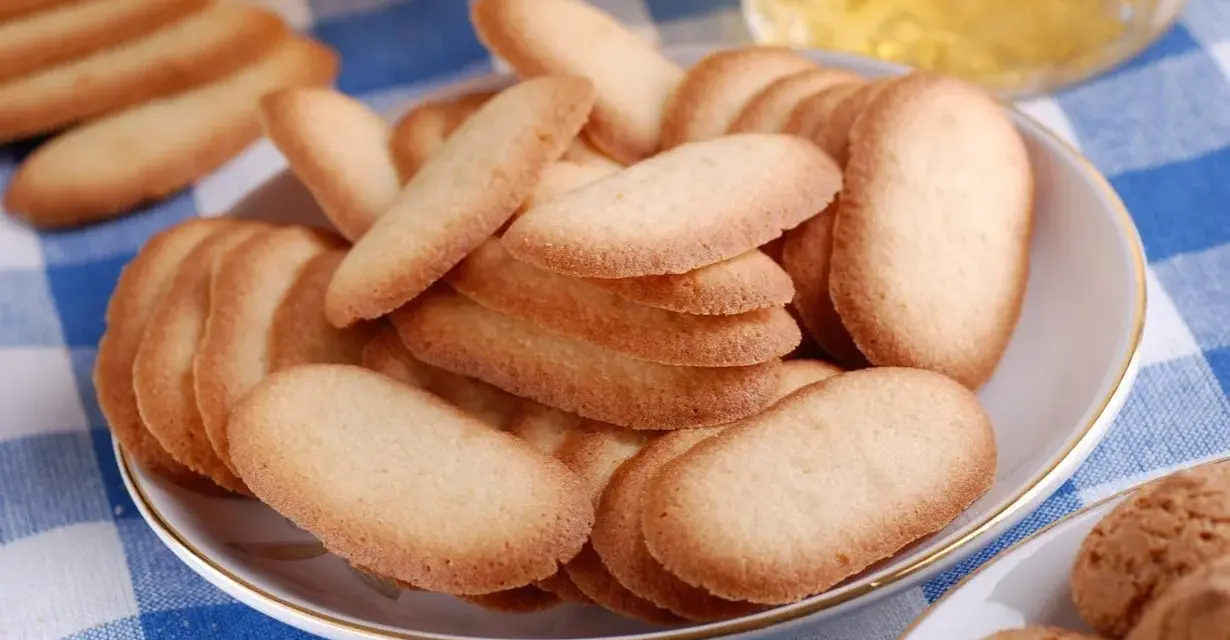 Un piatto pieno di croccanti lingue di gatto, perfette per accompagnare un tè o un caffè.