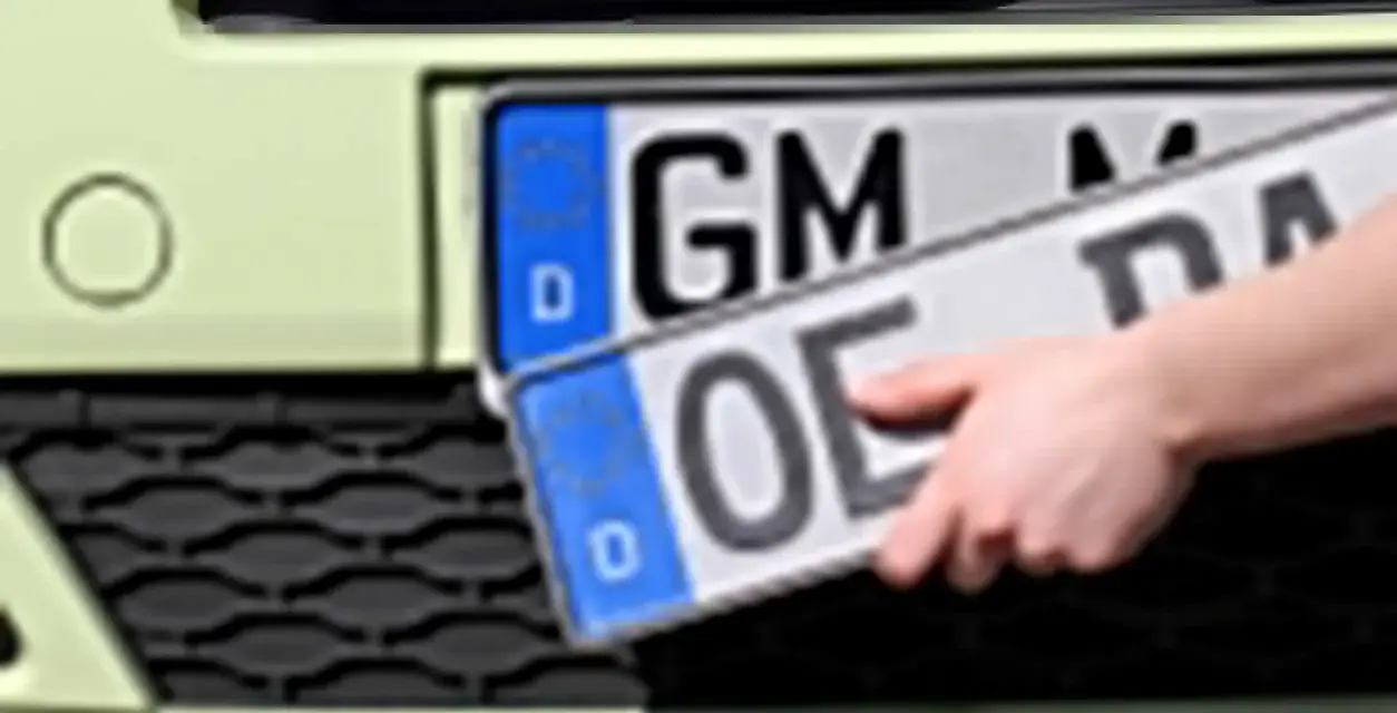 Dłoń trzyma niemieckie tablice rejestracyjne z literami "OE" i "GM".