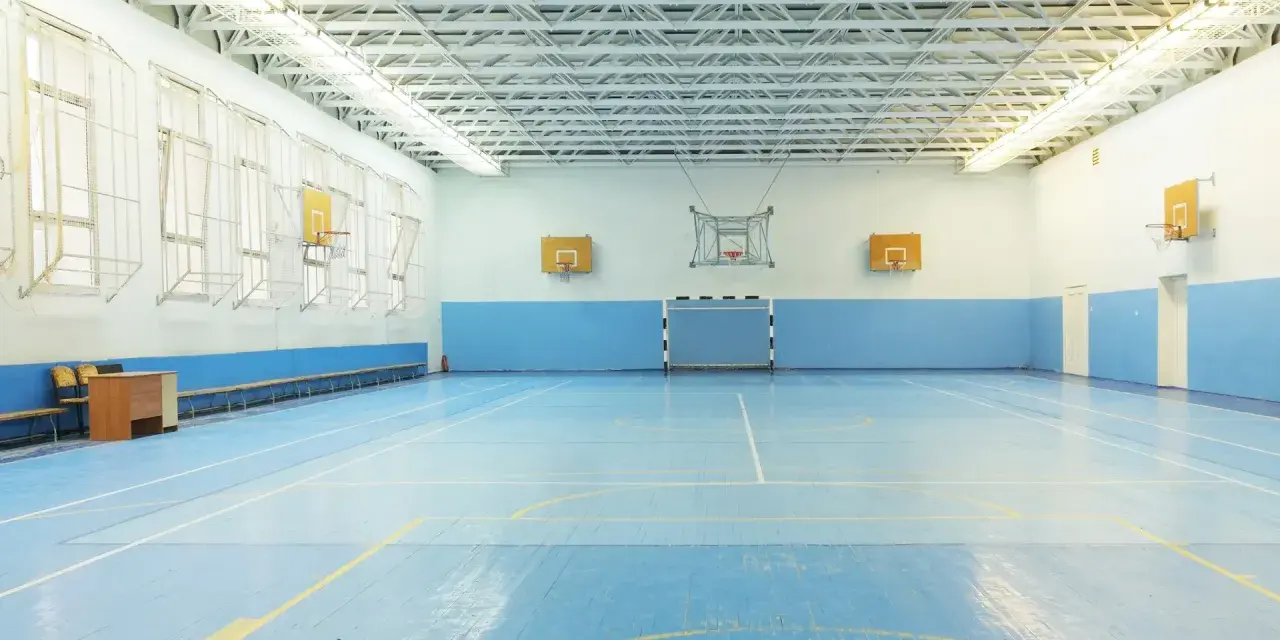 Pusta sala gimnastyczna z niebieską podłogą, boiskiem do koszykówki i piłki ręcznej. Idealne miejsce na zawody sportowe z doskonałym nagłośnieniem sali gimnastycznej.