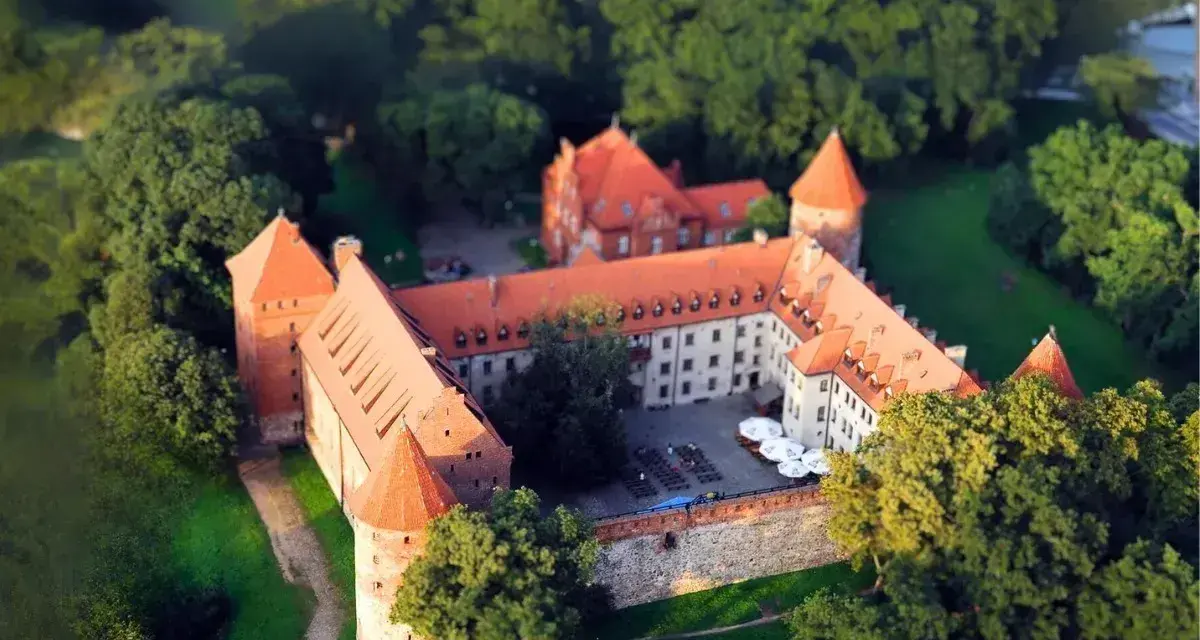 Zamek w Bytowie otoczony zielenią, z czerwonymi dachami i kamiennymi murami, wygląda jak z bajki.