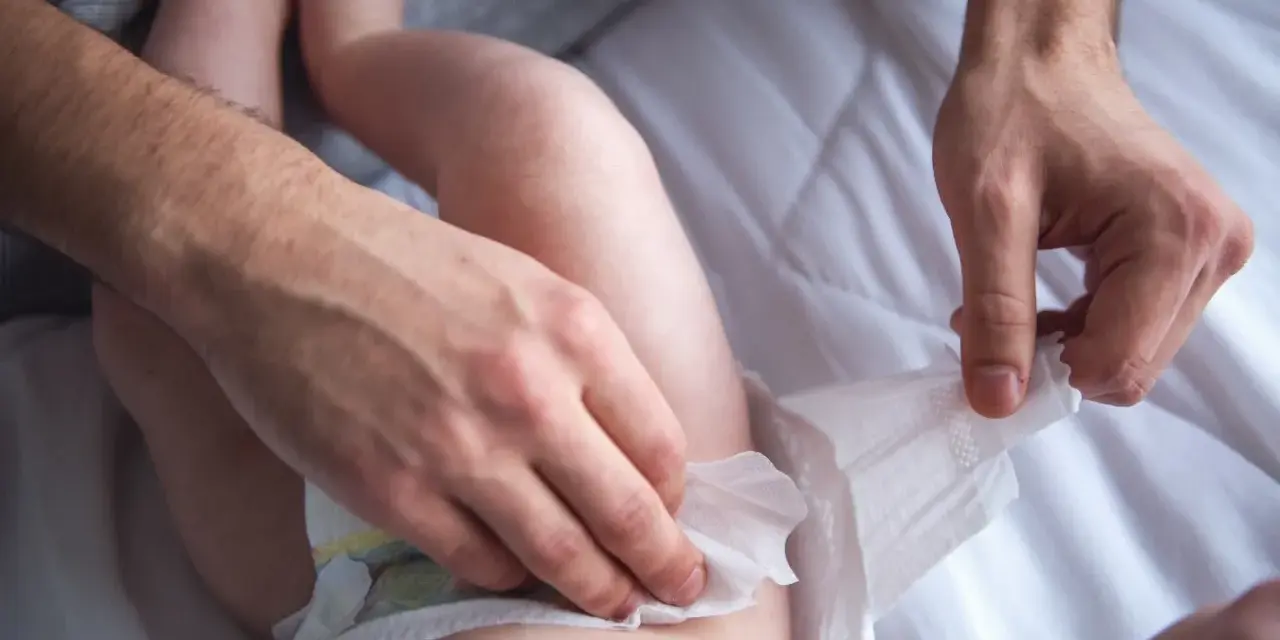 Ojciec zmienia pieluszkę dziecku. Ile pampersów dziennie zużywa niemowlę? To pytanie nurtuje wielu rodziców.