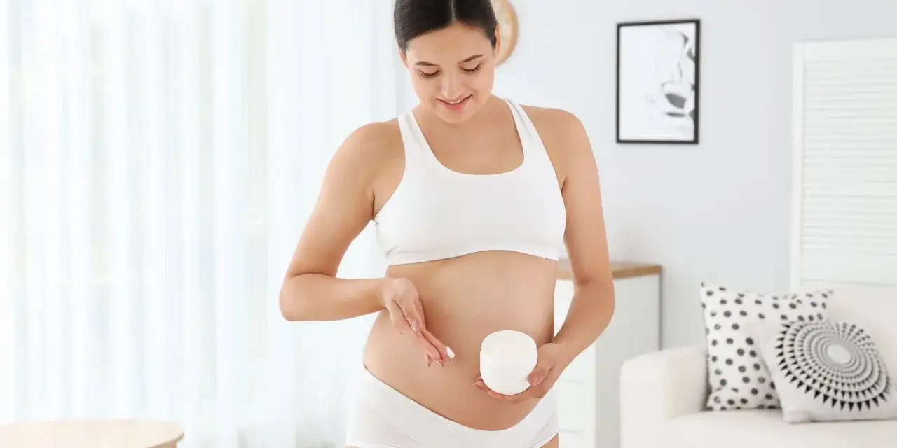 Kobieta w ciąży smaruje brzuch kremem, łagodząc swędzenie skóry.