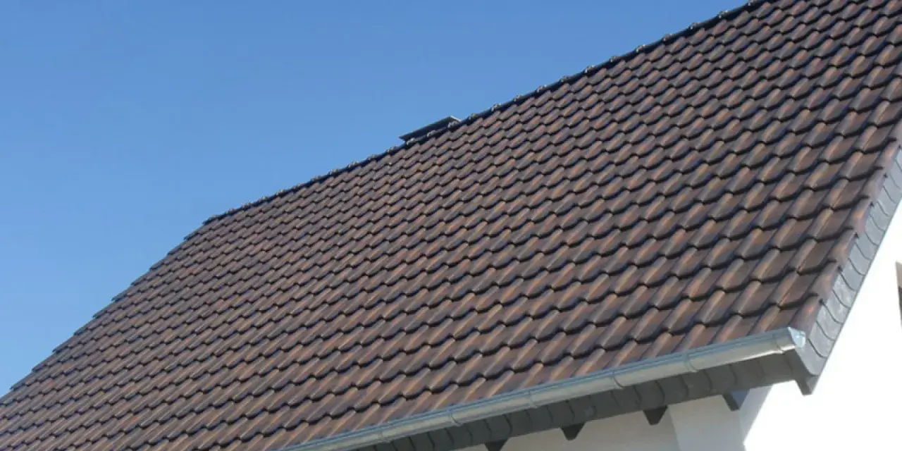 Dachówki ceramiczne na dachu domu, z widocznym okapem. Okap jest kluczowy, by wiedzieć, ile powinien wystawać dach poza ścianę, chroniąc ją przed deszczem.