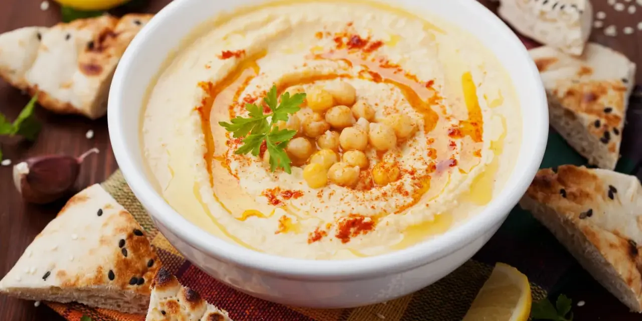 Un bol de houmous maison, garni de pois chiches, de persil et de paprika, servi avec du pain pita, du citron et de l'ail.