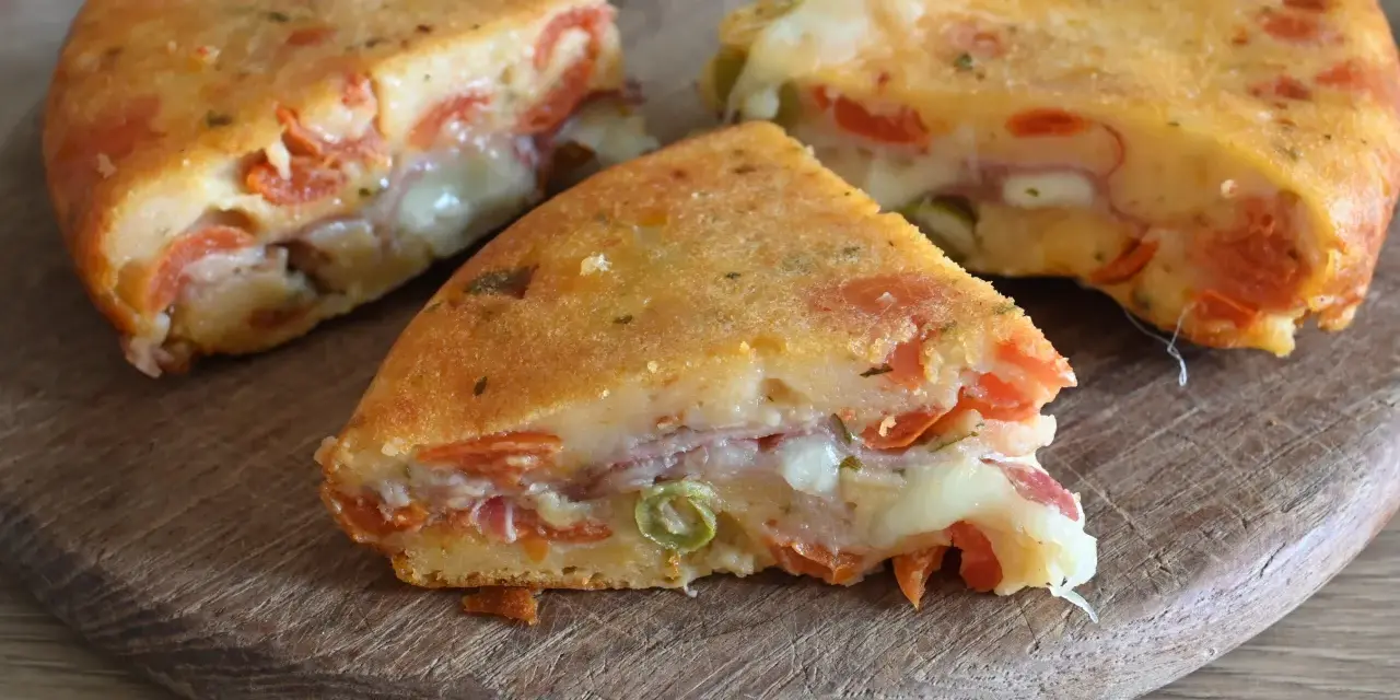 Fette di torta salata senza uova, ricca di pomodoro, formaggio filante e prosciutto, su un tagliere di legno.