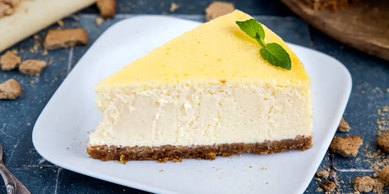 Ein cremiges Stück New York Cheesecake mit einem Keksboden, garniert mit Minze.