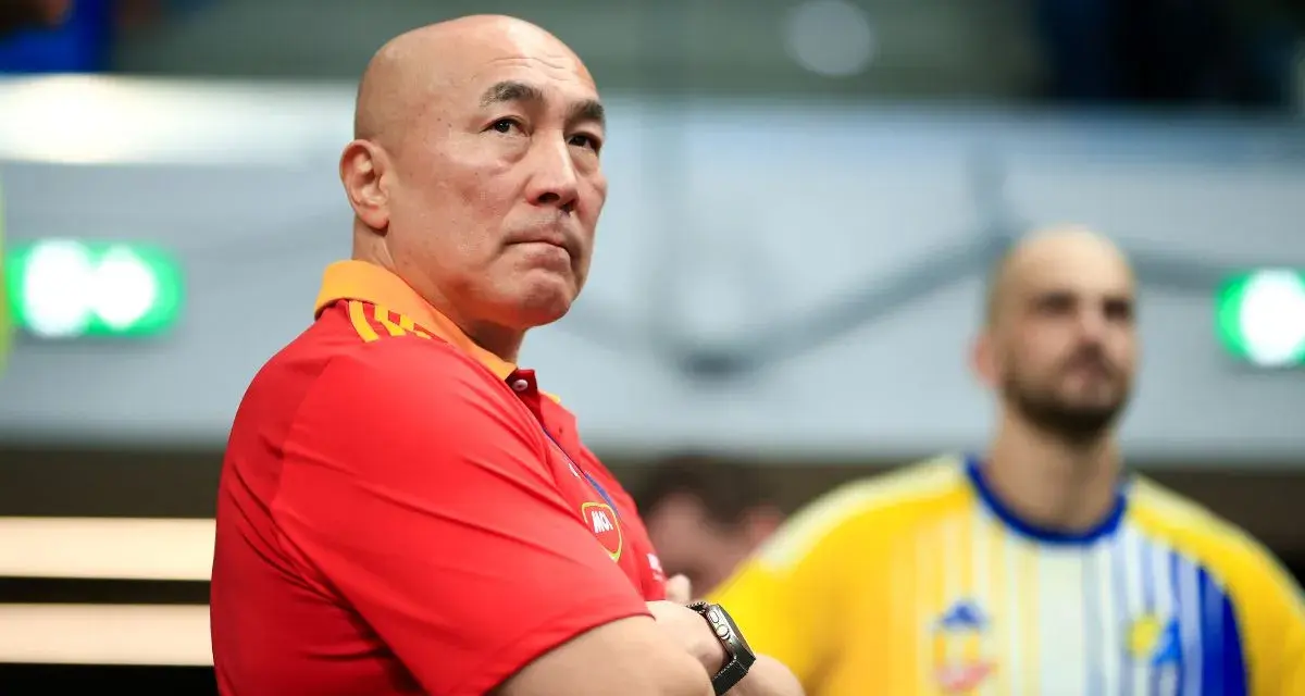 Skupiony trener Vive Kielce w czerwonej koszulce z pomarańczowym kołnierzem, z rękami skrzyżowanymi na piersi.