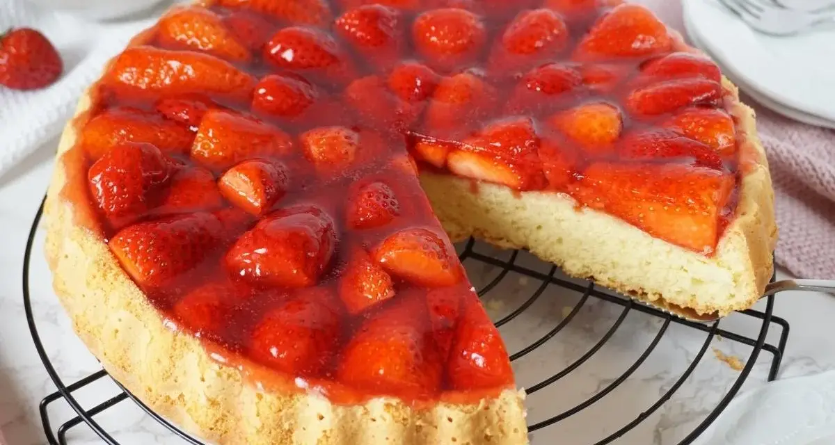 Ein saftiger tortenboden mit erdbeeren, bedeckt mit glänzendem Tortenguss. Ein Stück wurde bereits entnommen, um die köstliche Füllung zu zeigen.