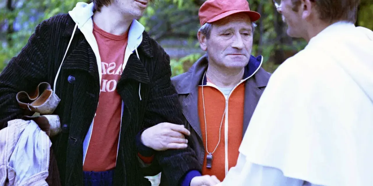 Czesław Nogacki w rozmowie z mężczyzną w białej szacie i z mężczyzną w czerwonej czapce.