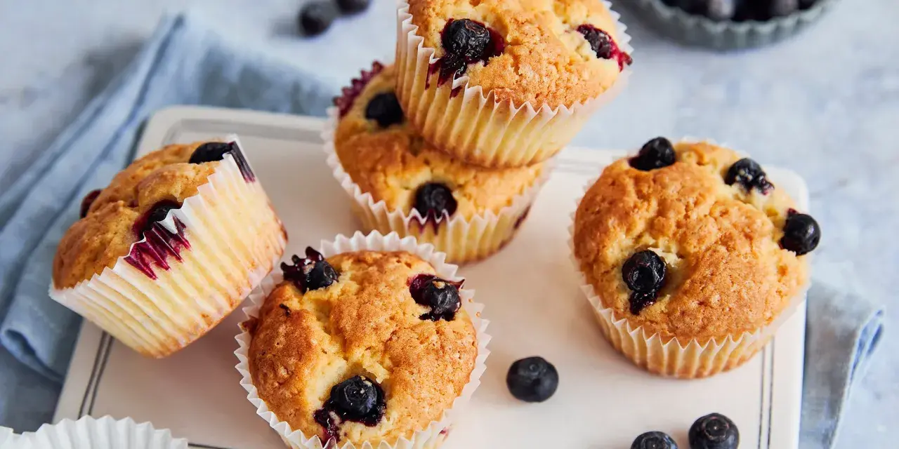 Saftige vegane Blaubeermuffins mit frischen Blaubeeren, auf einem weißen Teller mit blauer Serviette.