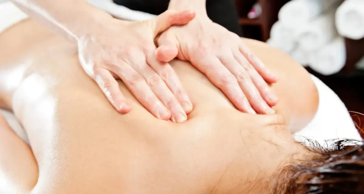 Hands perform a relaxing massage on a person's back, evoking the gentle pressure of shiatsu massage vs deep tissue.