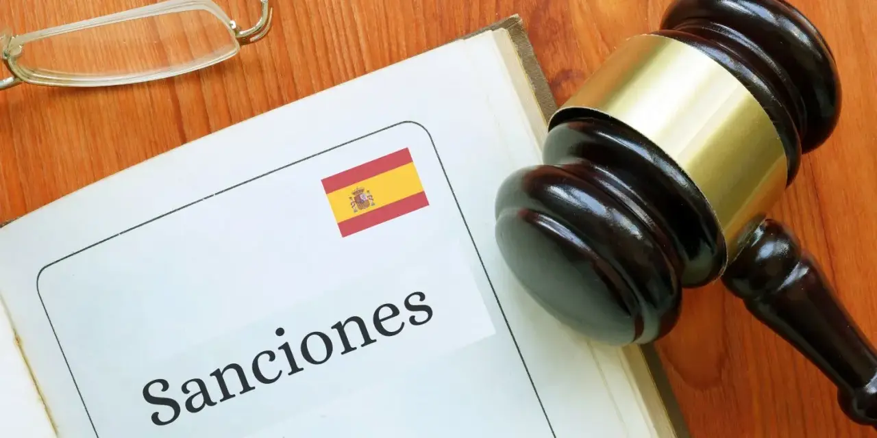 Martillo de juez sobre libro abierto con la palabra "Sanciones" y la bandera de España. Podría ser una multa hacienda.