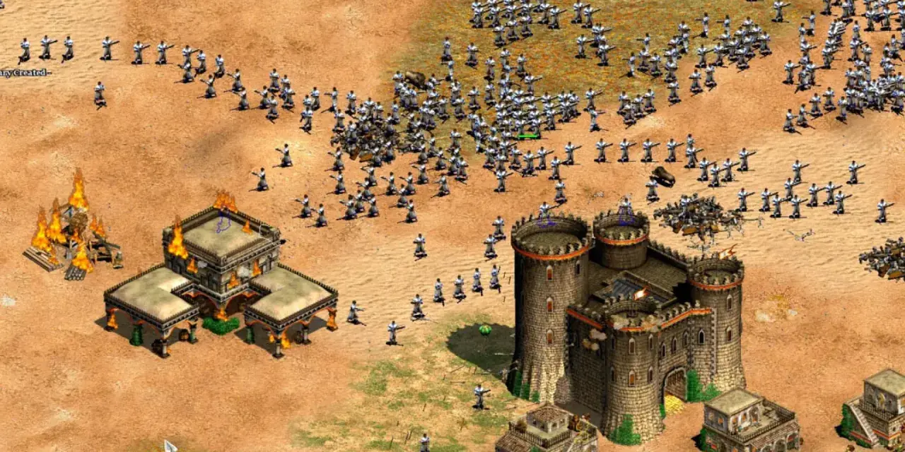Un ejército avanza en Age of Empires 3, con edificios en llamas y un castillo imponente. ¡Descubre trucos para dominar el campo de batalla!