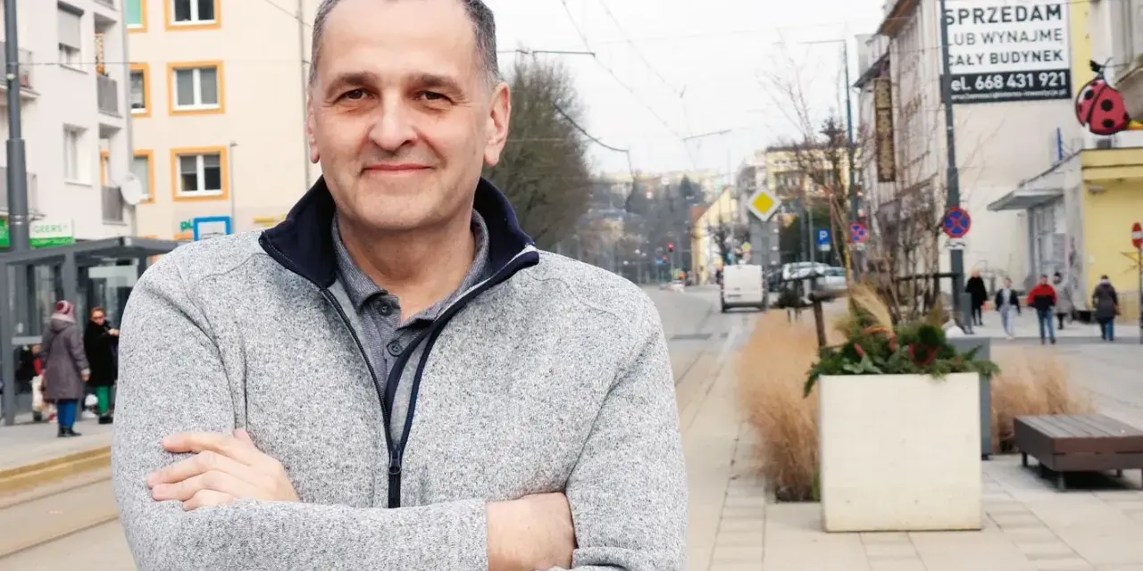 Sebastian Pieńkowski stoi na tle miejskiej ulicy z tramwajami i budynkami.