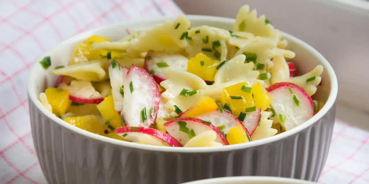 Ein bunter Nudelsalat mit Farfalle, Radieschen und gelben Paprikawürfeln, garniert mit Schnittlauch. Perfekt für den Sommer!