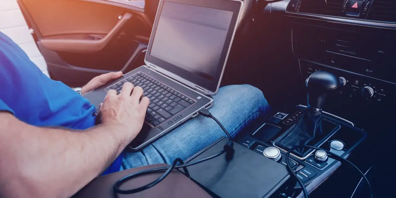 Mężczyzna w samochodzie podłącza laptopa do zasilania, pokazując, jak podłączyć komputer do samochodu.