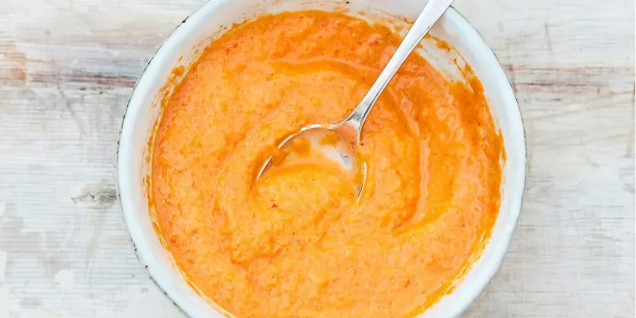 Eine Schüssel mit cremiger, orangefarbener mojo rojo Sauce, die mit einem Löffel umgerührt wird.