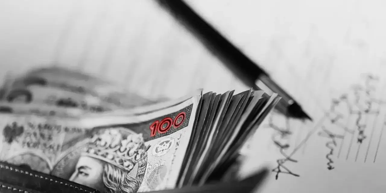Stos banknotów 100 zł w portfelu, obok długopis i dokumenty. Może to być umowa, gdzie kara umowna jest zapisana.