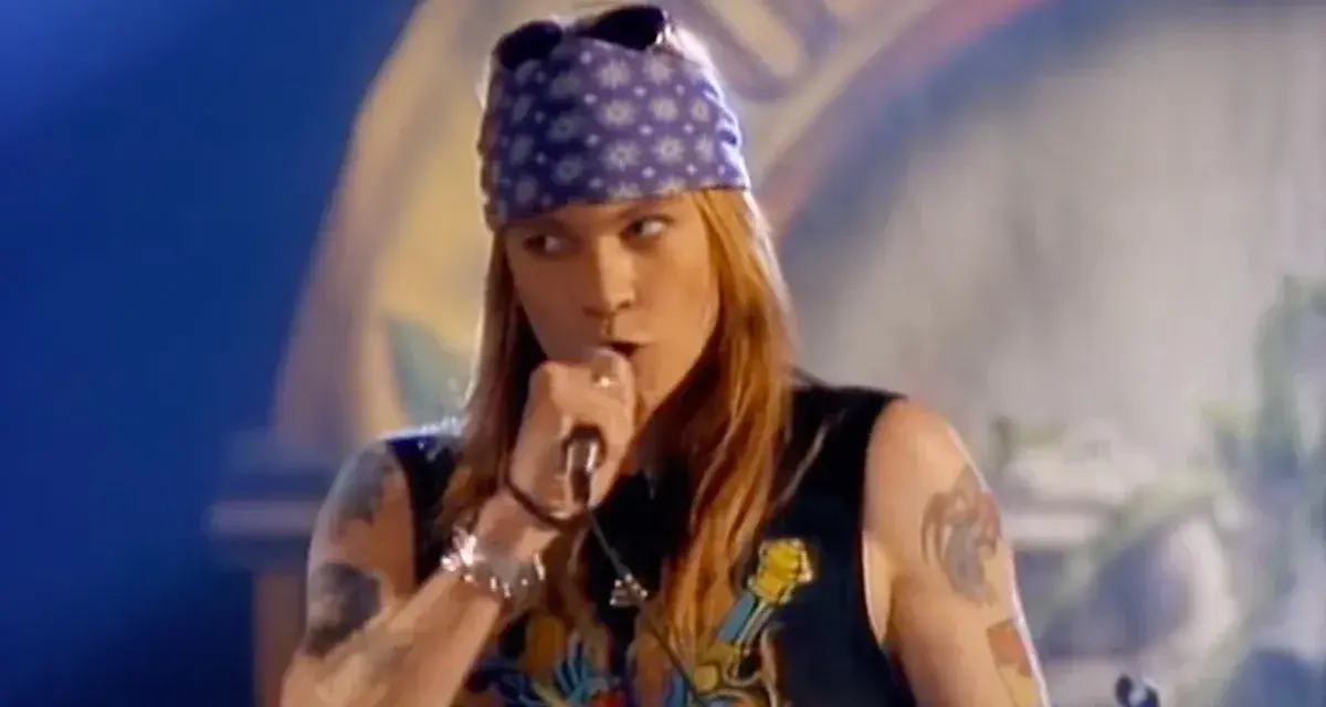 Axl Rose w fioletowej bandanie i czarnej koszulce śpiewa do mikrofonu, jakby dedykował "sweet child o' mine" publiczności.