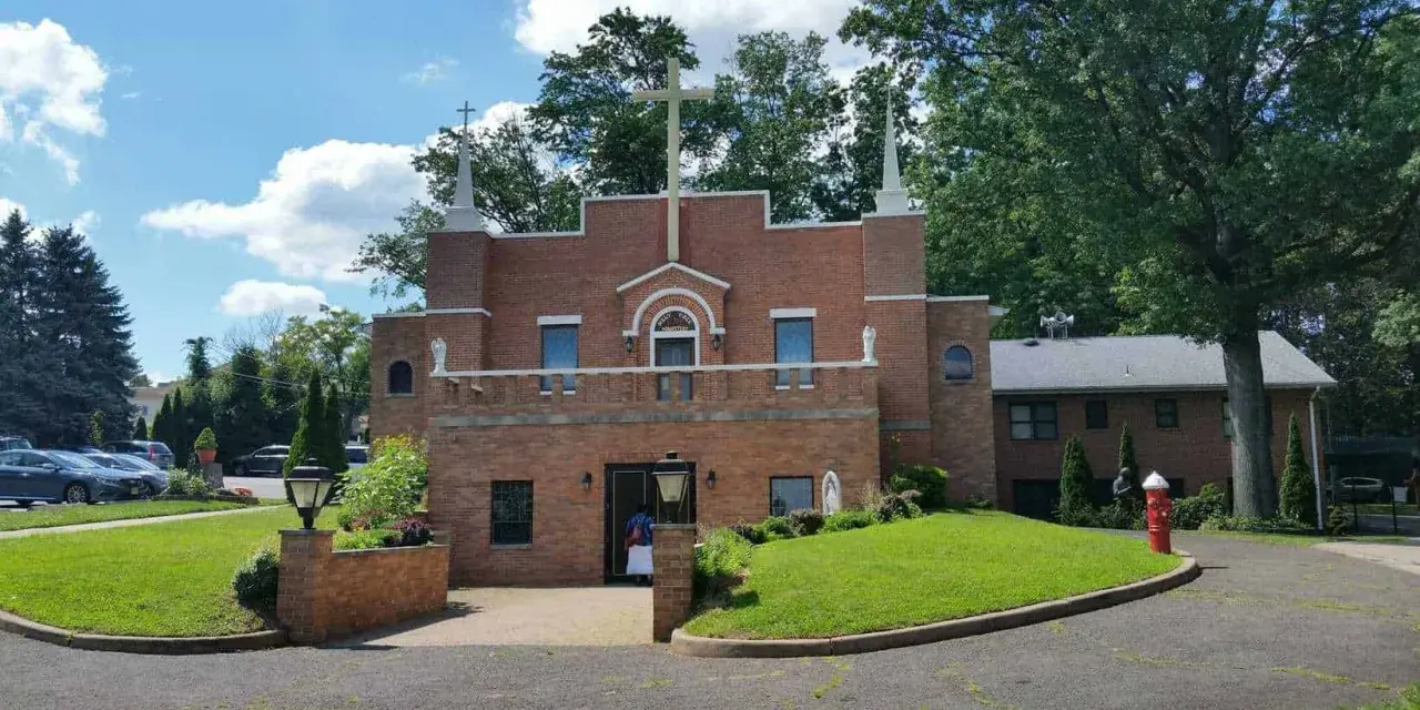 The Holy Face Monastery, a brick building with a large cross, stands on a sunny day.
