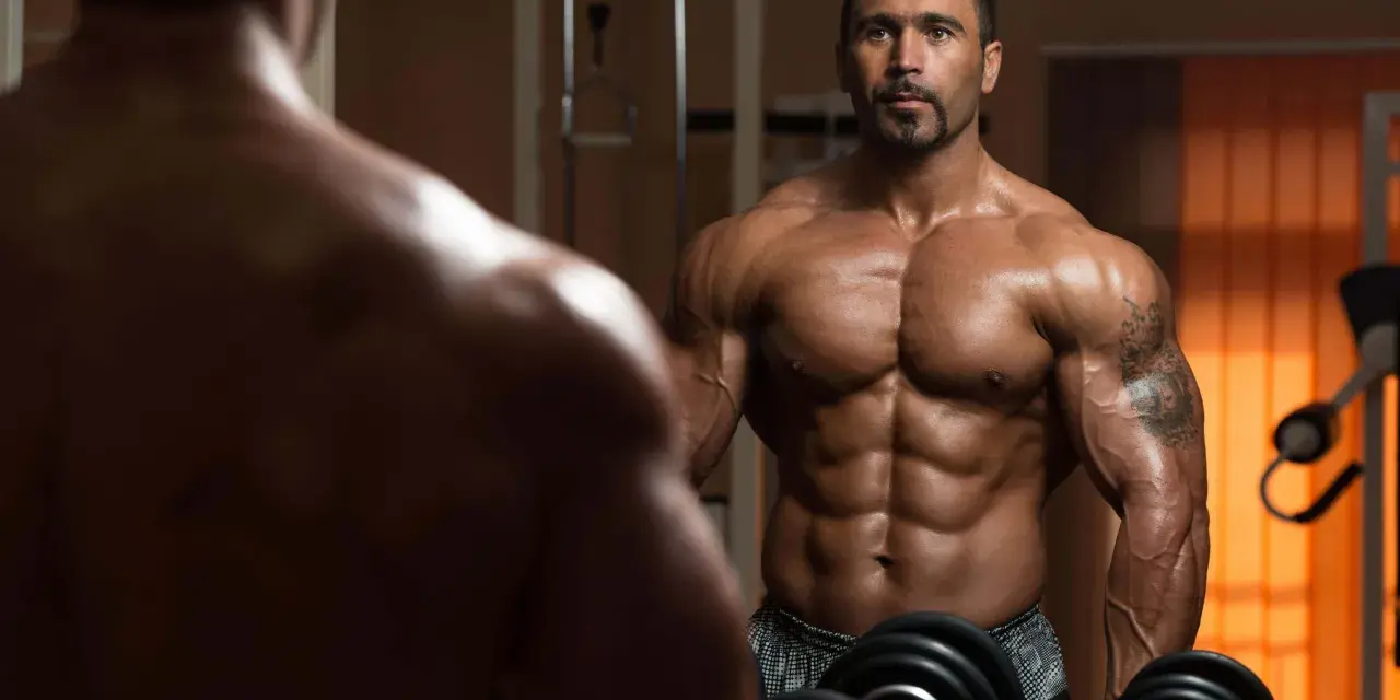Muskulös man i gym speglar sig. Hans resa att gå ner i vikt och bygga muskler syns tydligt.