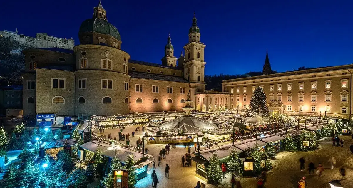 A magical Salzburg Austria Christmas market glows at night, with stalls, trees, and the cathedral creating a festive scene.