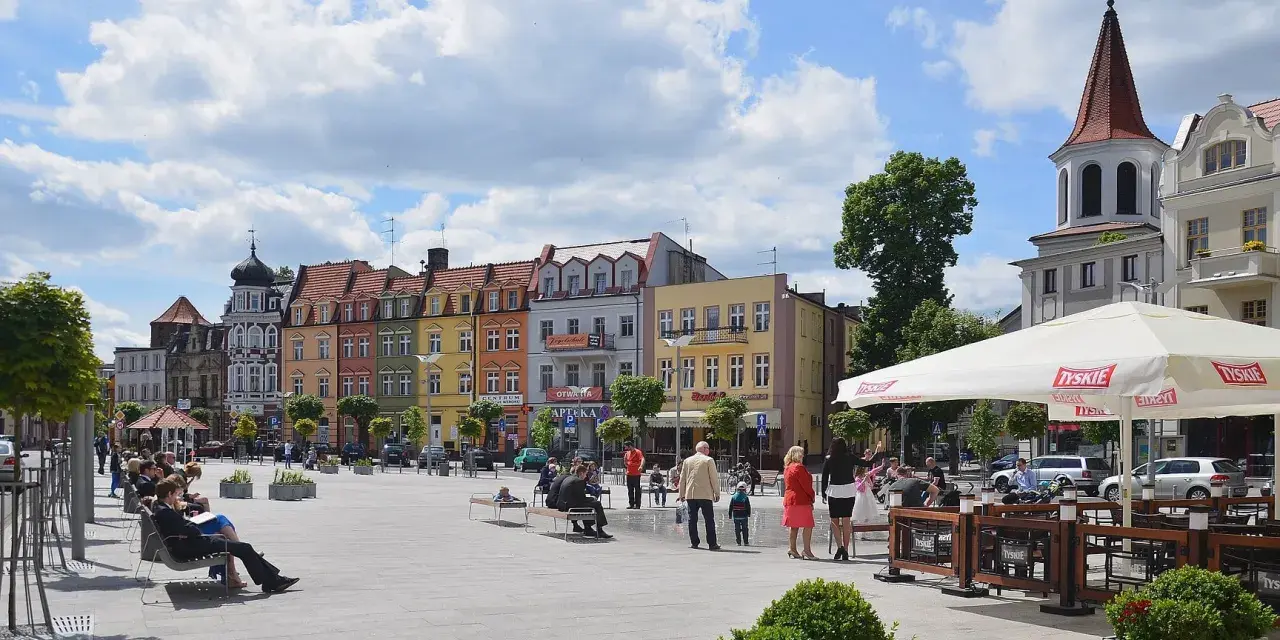 Kolorowy brodnica rynek tętni życiem. Ludzie odpoczywają na ławkach, a kawiarniany ogródek zaprasza do relaksu pod białym parasolem.