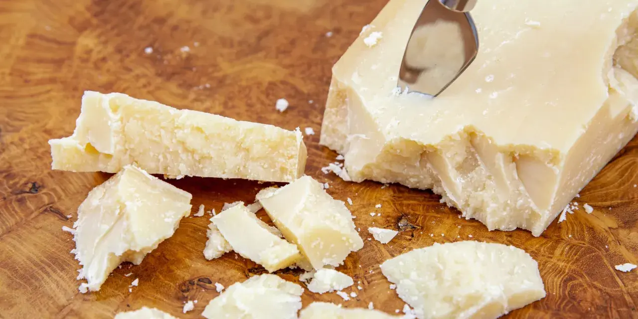Kawałki Grana Padano na drewnianej desce, gotowe do posypania makaronu lub dodania do sosów.