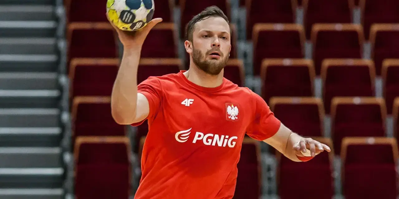 Mateusz Przybylski w czerwonej koszulce z orłem i logo PGNiG, gotowy do rzutu piłką ręczną.
