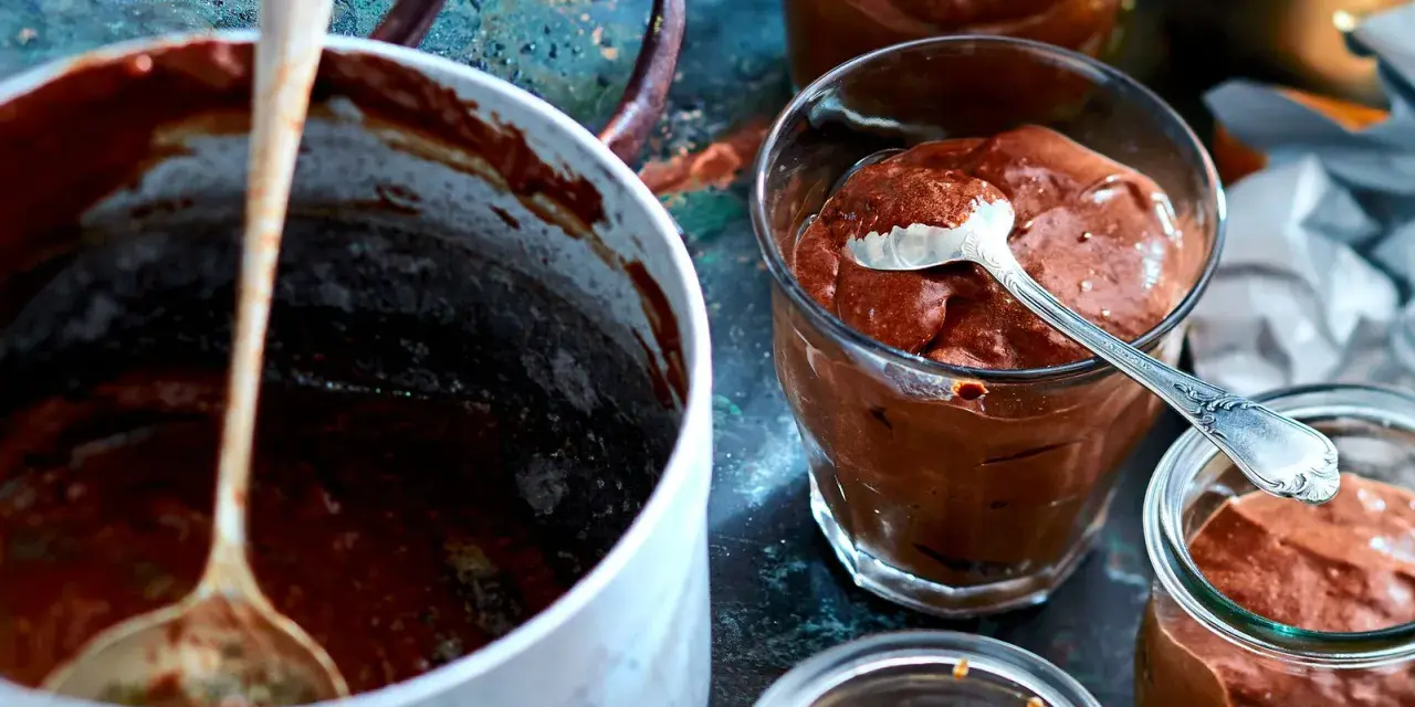 Omas schokoladenpudding mit sahne, cremig und köstlich in Gläsern serviert. Ein Löffel wartet schon.